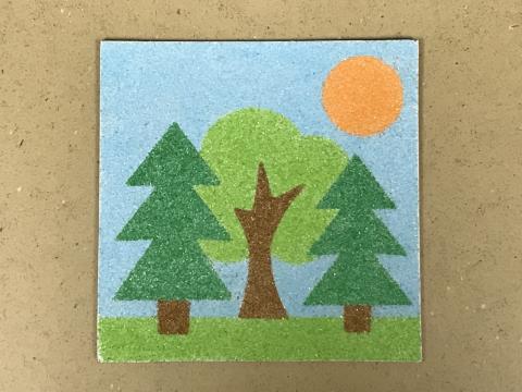 a flat sand art piece featuring trees and the sun