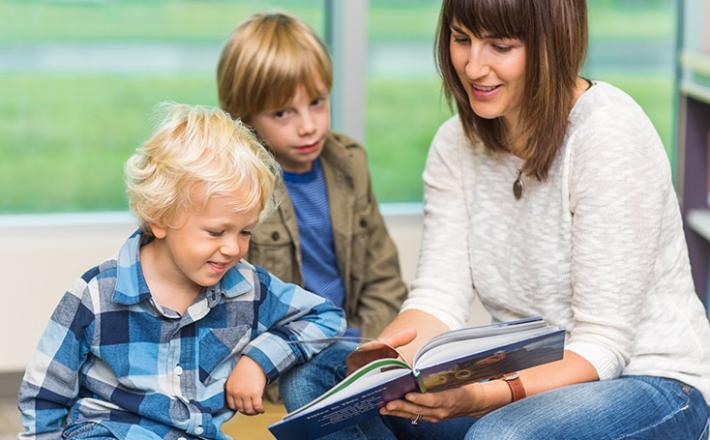 woman reading book to two boys in a library