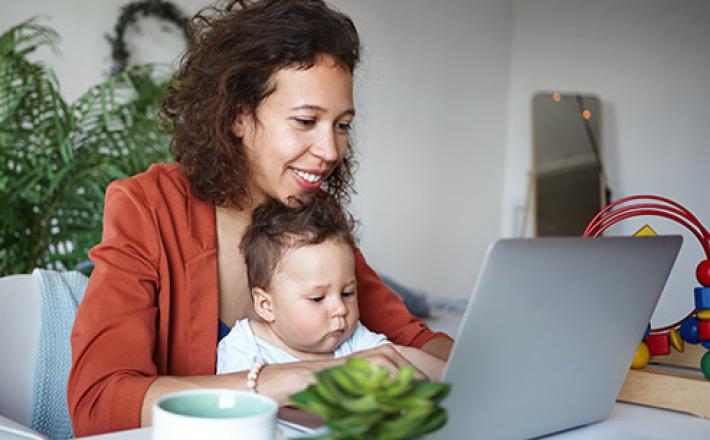 Woman using a laptop with baby on her lap.